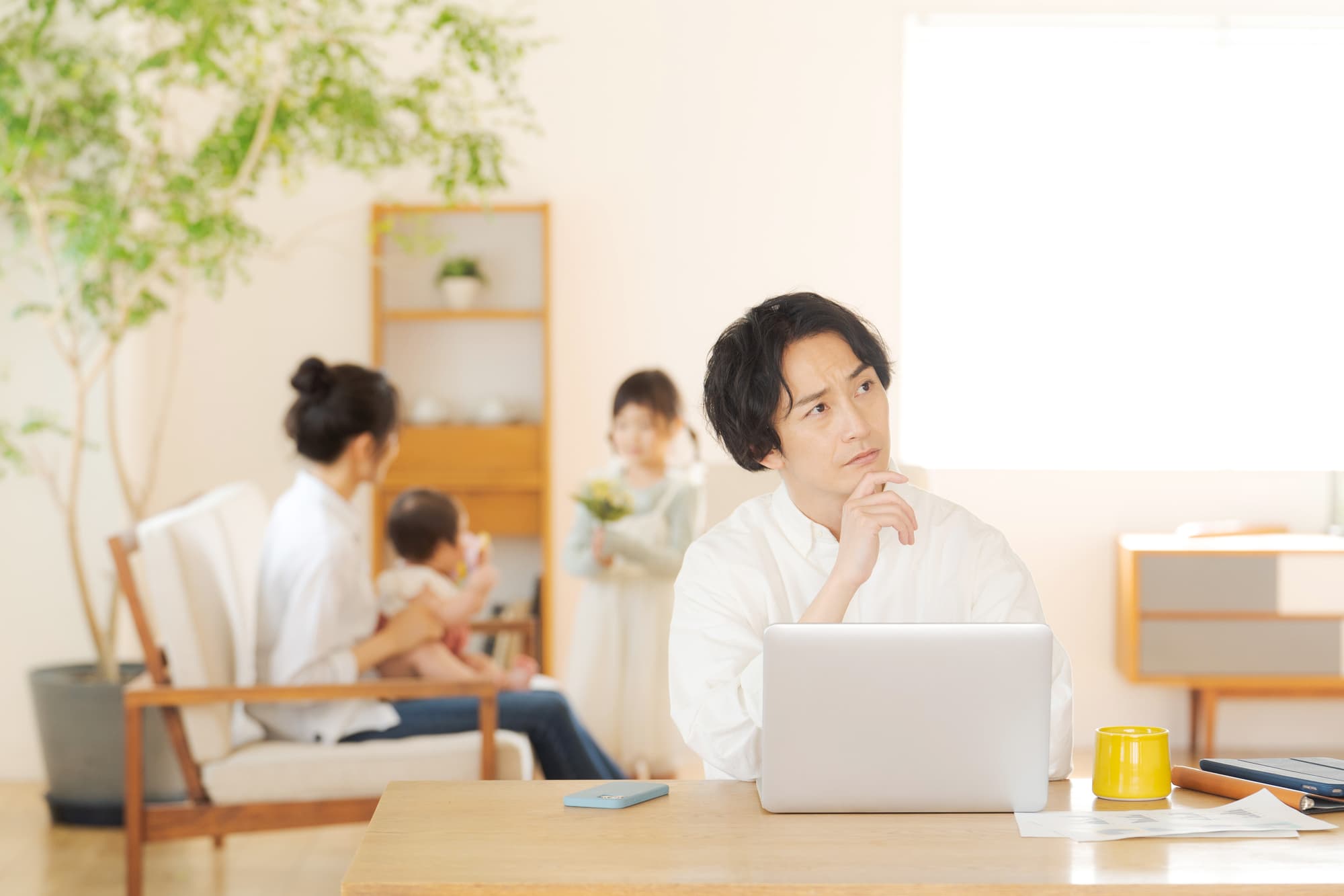 リビングで遊ぶ子供と母親のそばでパソコンを広げ子どもの歯並びについて調べる父親