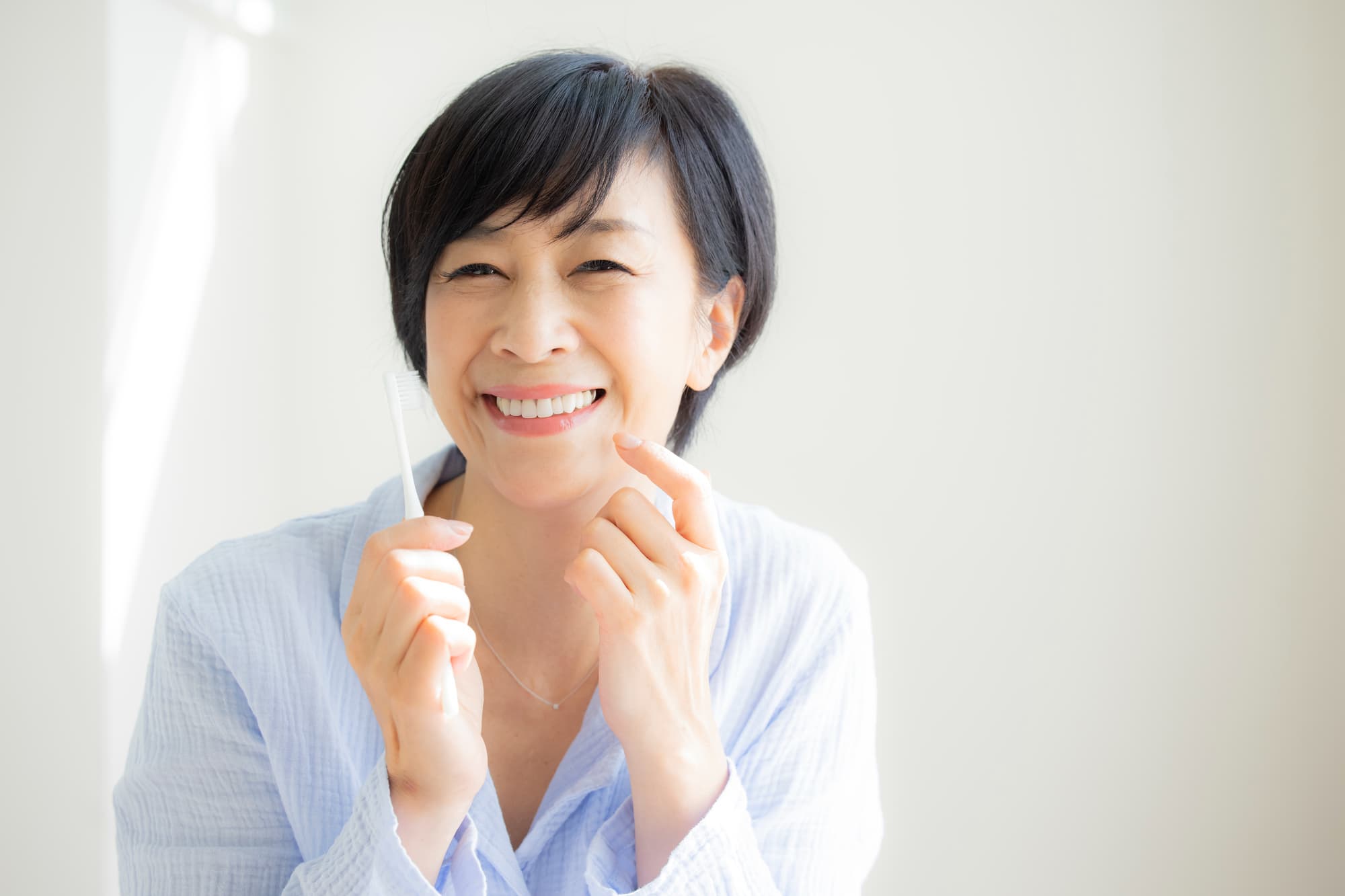 インプラント治療をした歯を指さして笑顔を見せる女性