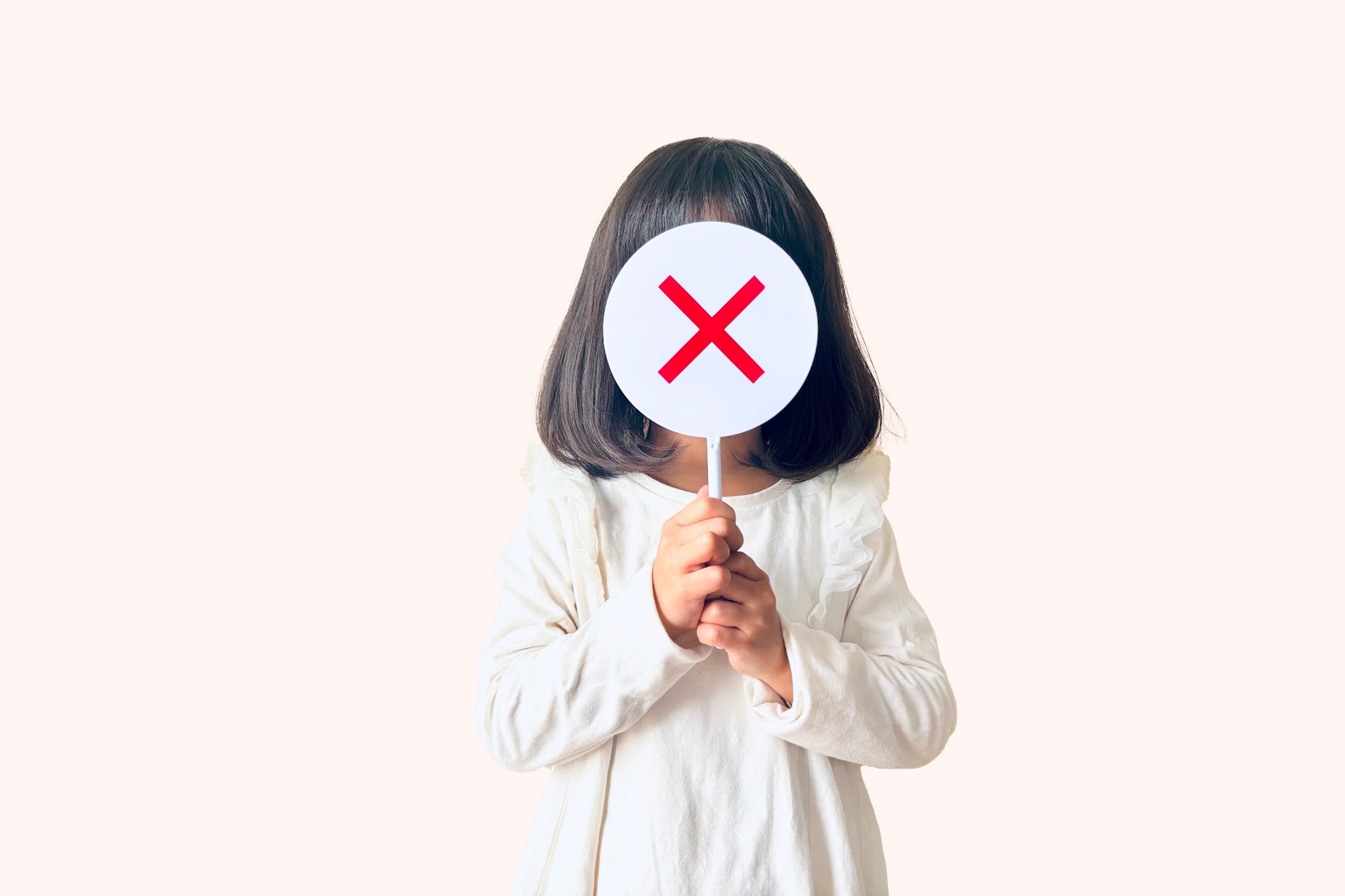 小児矯正が1期のみで終わらないとバツマークを顔の前に掲げる子ども